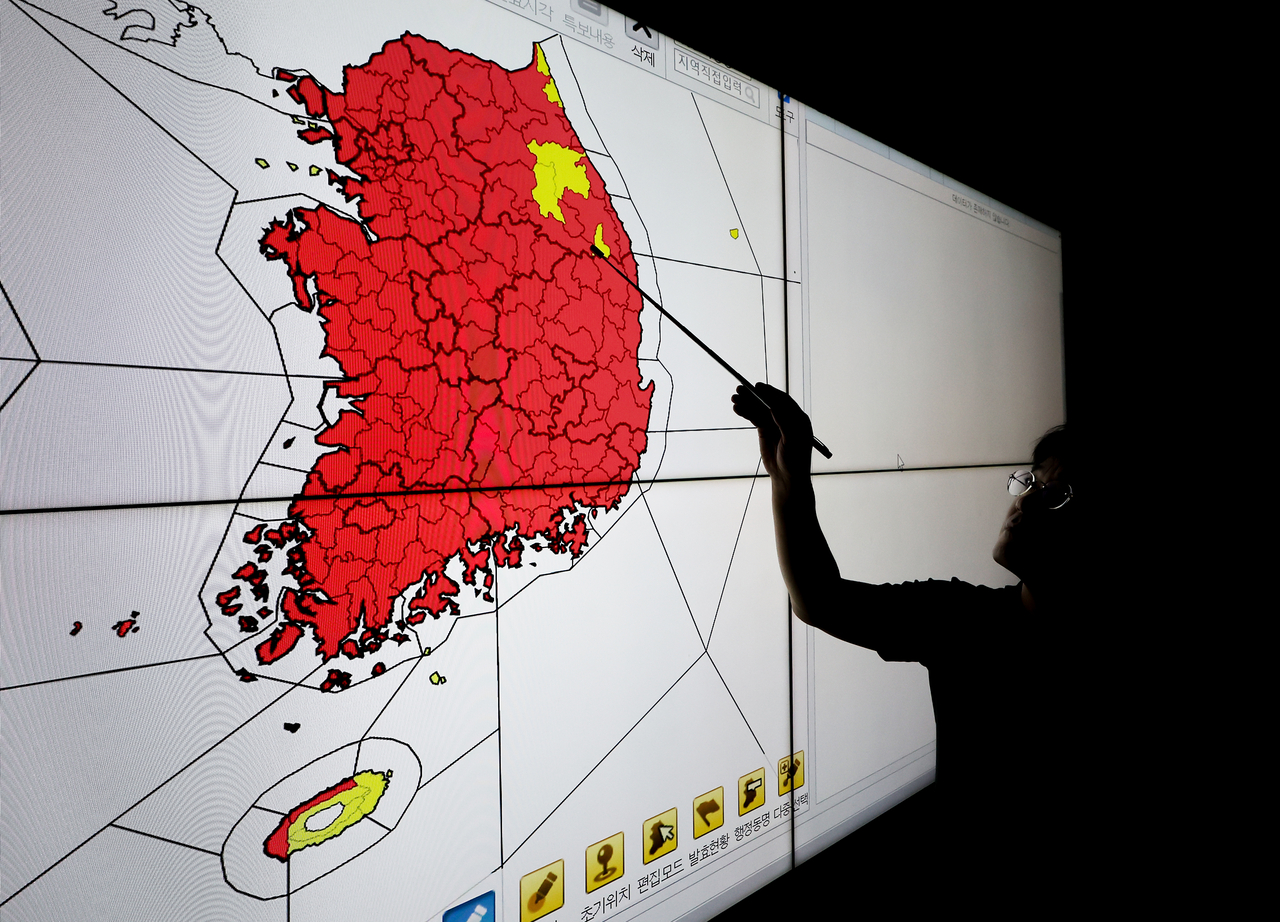 This file photo shows a weather agency official pointing to a map of South Korea, with areas under a special heat wave advisory marked in red across most of the country on July 30. (Yonhap)