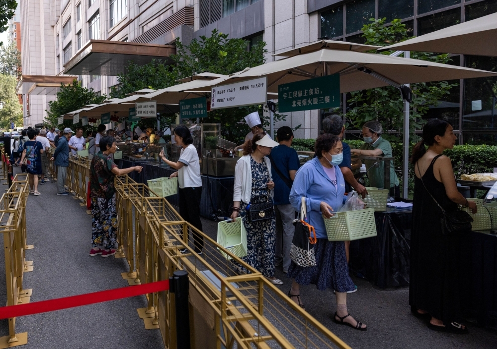 Chinese hotels turn to hawking food as guests tighten belts. People gather near a setup of stalls selling food to passersby next to Beiyuan Grand Hotel in Beijing August 11, 2025. [Reuters]