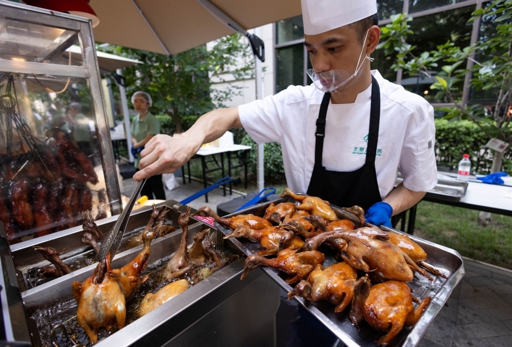A chef fries pigeons in hot oil in a metal fryer at a setup of stalls selling food to passersby next to Beiyuan Grand Hotel in Beijing August 11, 2025.  [Reuters]