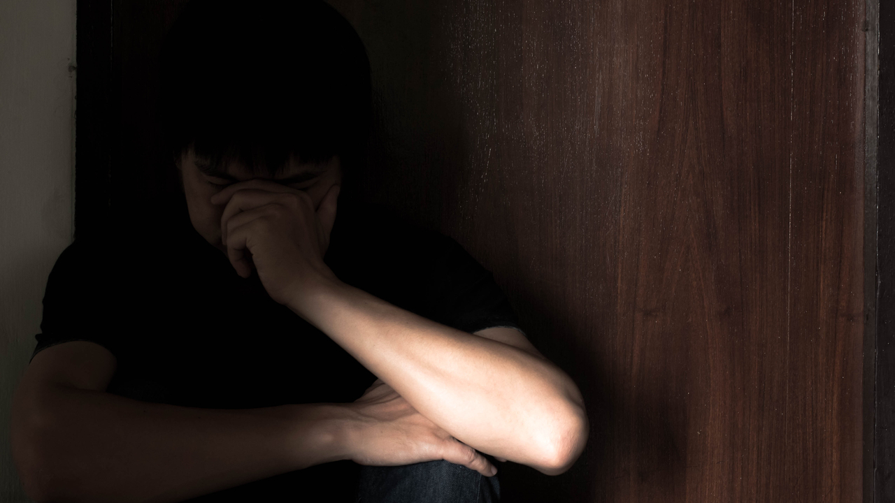 A boy sits in the dark leaning against the door (123rf)