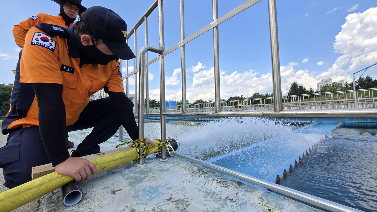 A firefighter holds a hose steady as water is pumped into the Hongje Water Purification Plant, in Gangneung on Sunday. (Yonhap)
