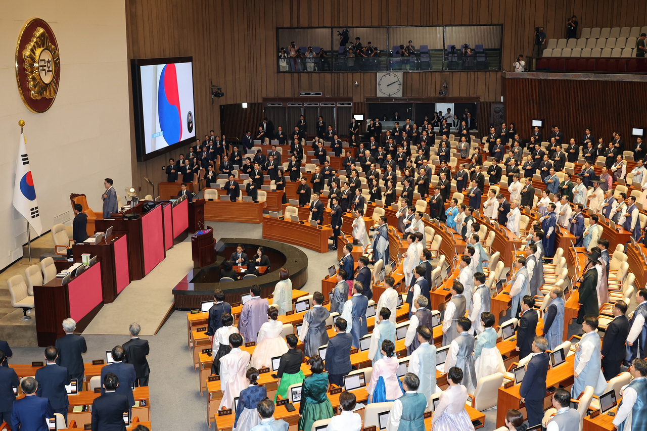 Ruling party lawmakers wearing hanbok and main opposition lawmakers in mourning attire salute the national flag during the opening of the regular parliamentary session at the National Assembly in Yeouido, Seoul, Monday. Hanbok was suggested by Assembly Speaker Rep. Woo Won-shik of the ruling Democratic Party, while lawmakers from the main opposition People Power Party wore black in protest against the ruling bloc. (Yonhap)