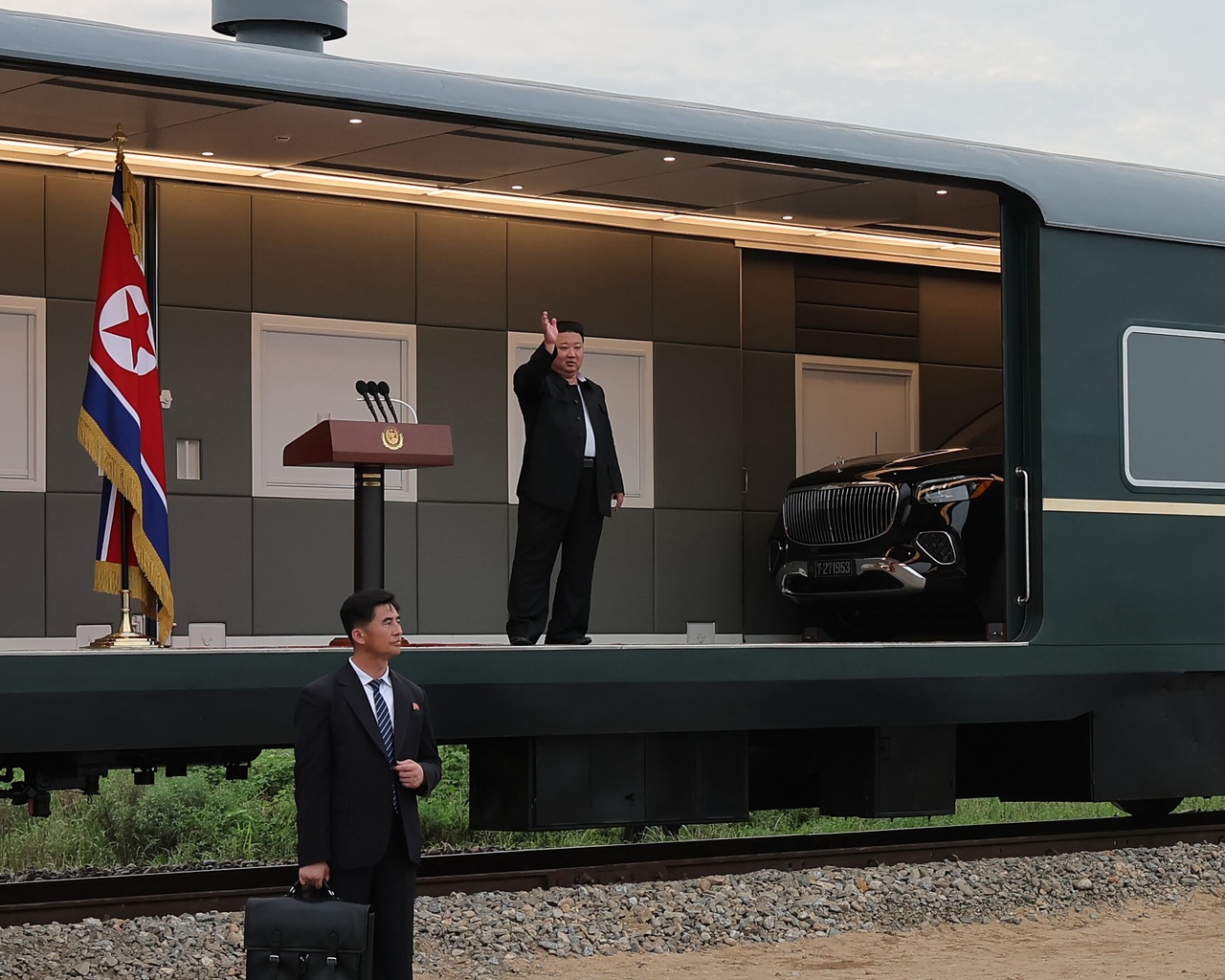 North Korean leader Kim Jong-un (top) waves to local residents during a visit to flood-stricken Uiju County in North Pyongan Province in August 2024, with a vehicle believed to be a Mercedes-Maybach GLS 600 4Matic peeking out from inside his armored train. (Korean Central News Agency via Yonhap)