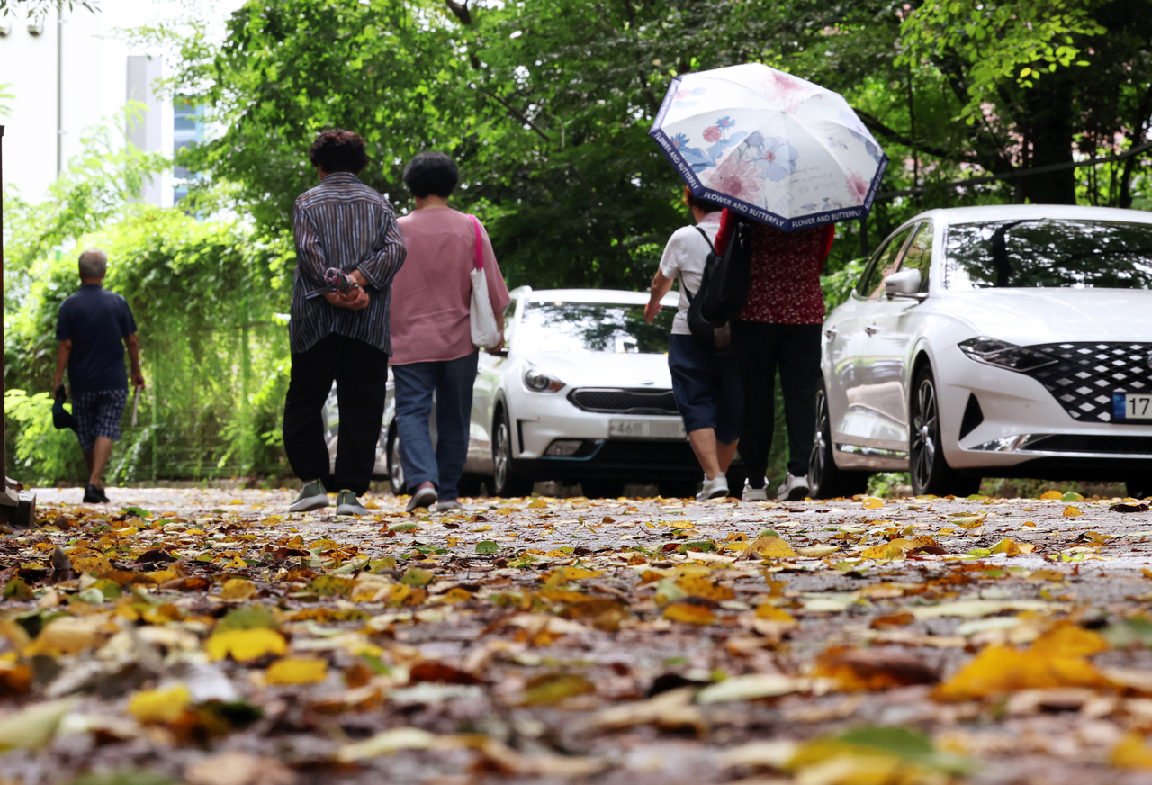 Pedestrians walk across a road covered with fall leaves at Jungwoe Park in Gwangju on Tuesday. (Yonhap)