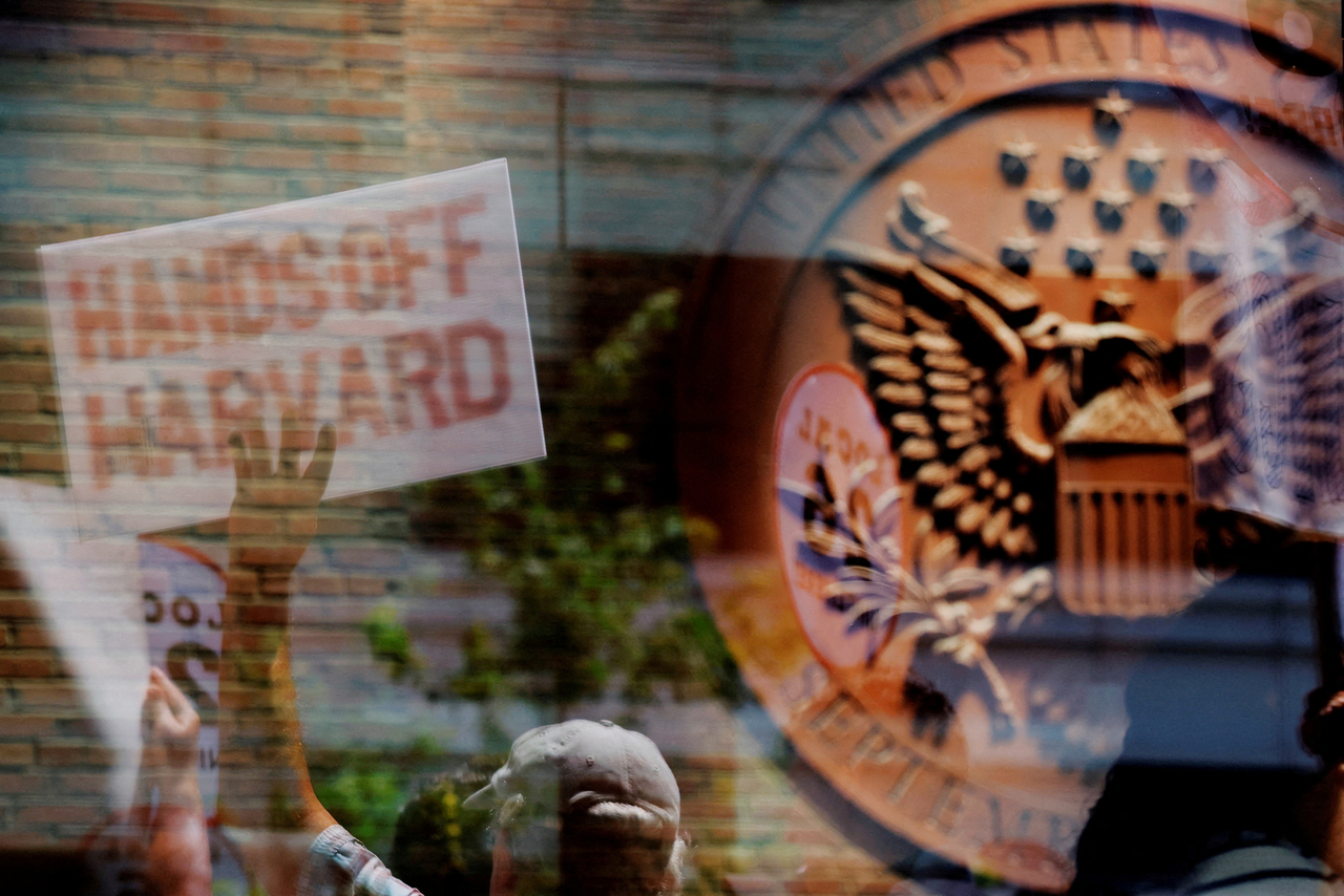 Demonstrators with group Crimson Courage, who gathered to support Harvard University outside a hearing before a federal judge to order US President Donald Trump's administration to restore about $2.5 billion in canceled federal grants and cease efforts to cut off research funding, are reflected in a window of the federal courthouse in Boston, Massachusetts, July 21.  Reuters-Yonhap