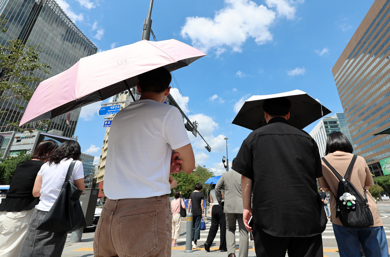 Pedestrians wait to cross the street with parasols at Jongno-gu, central Seoul on Aug. 22. (Newsis)