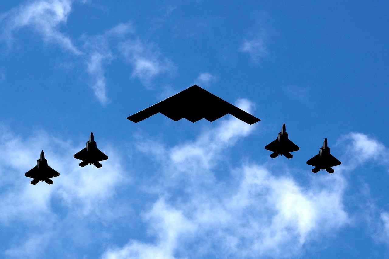 미 공군 소속 B-2 스피릿 스텔스 폭격기의 주변에 F-22 랩터 스텔스 전투기가 호위하며 비행하고 있다. [로이터]