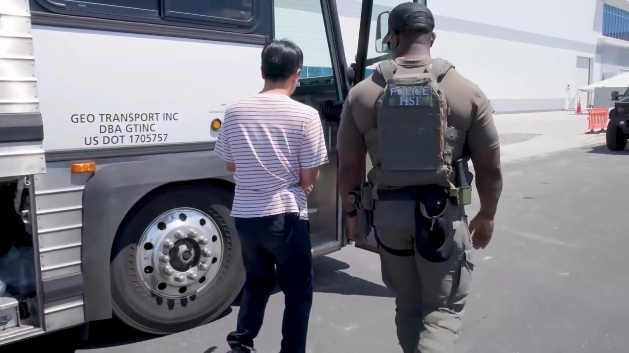 A screen capture from video released Friday by US Immigration and Customs Enforcement, under the Department of Homeland Security, shows an individual believed to be a South Korean, handcuffed and in chains, being escorted by a US immigration official to a bus during Thursday’s raid at an electric vehicle battery plant construction site in Georgia. (Screengrab from ICE video via The Korea Herald)