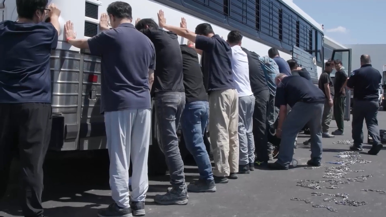 A screen capture from video released Friday by US Immigration and Customs Enforcement, under the Department of Homeland Security, shows individuals believed to be South Koreans standing against a bus as US immigration officials chain them during Thursday’s raid at an electric vehicle battery plant construction site in Georgia, being built by HL-GA Battery Company. (Screengrab from ICE video via The Korea Herald)