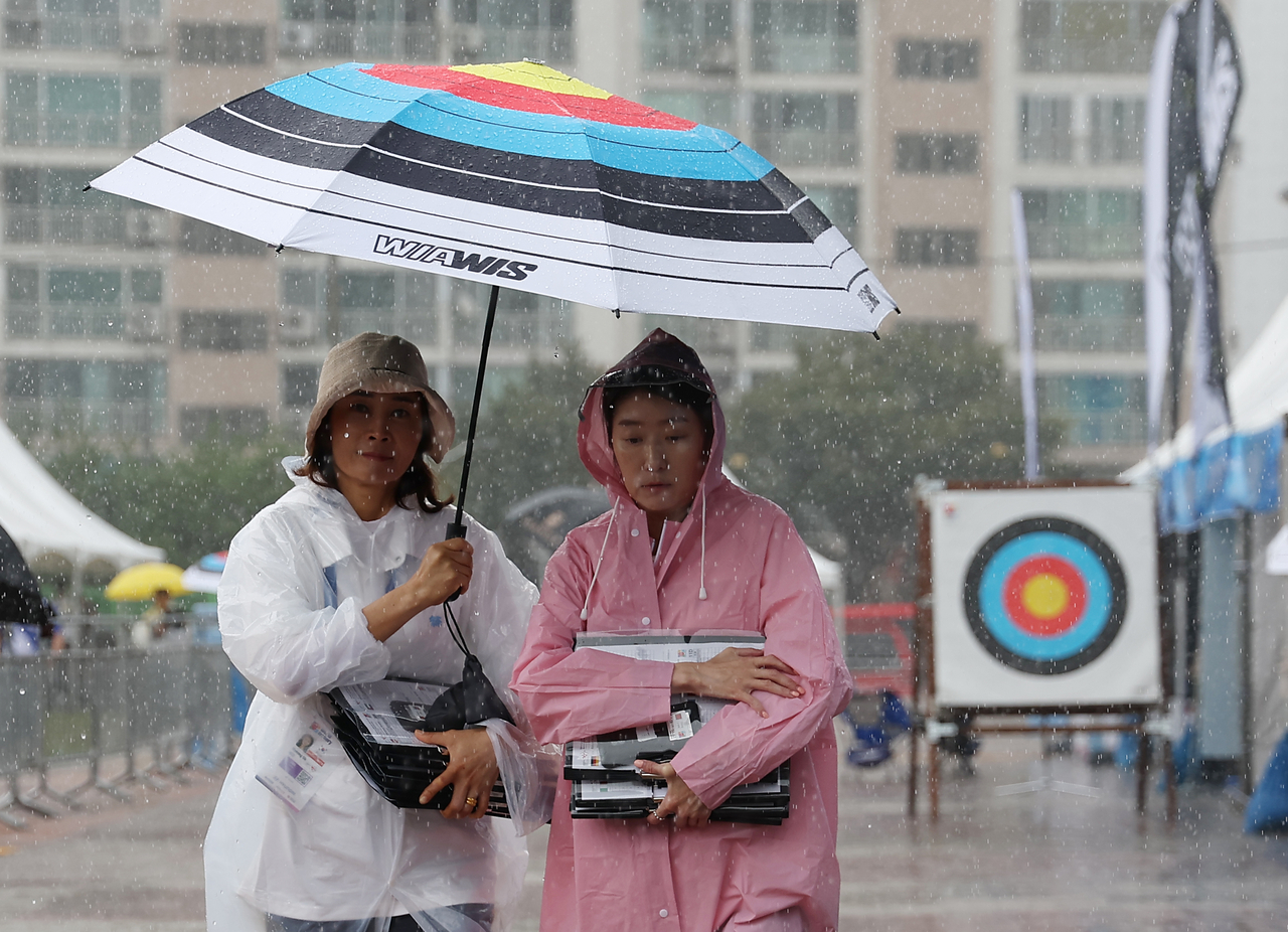 Officials share an umbrella during a sudden shower Tuesday at the Gwangju International Archery Center in Gwangju, during the preliminary round of the recurve individual event at the 2025 World Archery Championships. (Yonhap)
