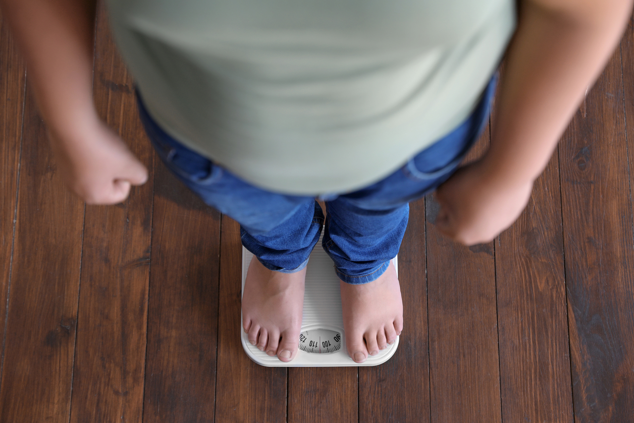 An overweight boy stands on a scale.   123rf
