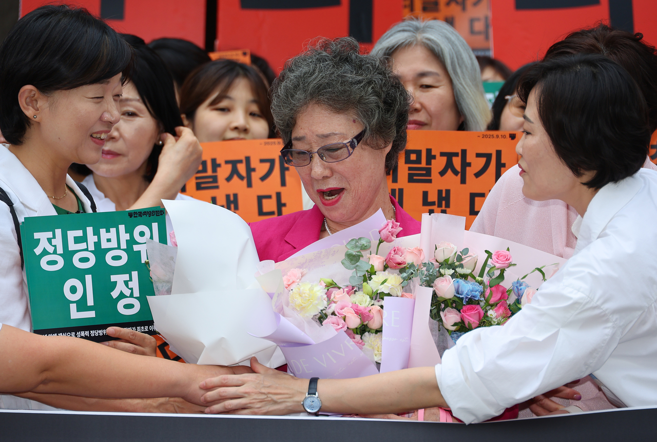 Choi Mal-ja, who was convicted for biting off the tongue of a man attempting to sexually assault her in 1964, receives flower bouquets outside a Busan court on Wednesday after a retrial acquitted her, overturning the original conviction. (Yonhap)