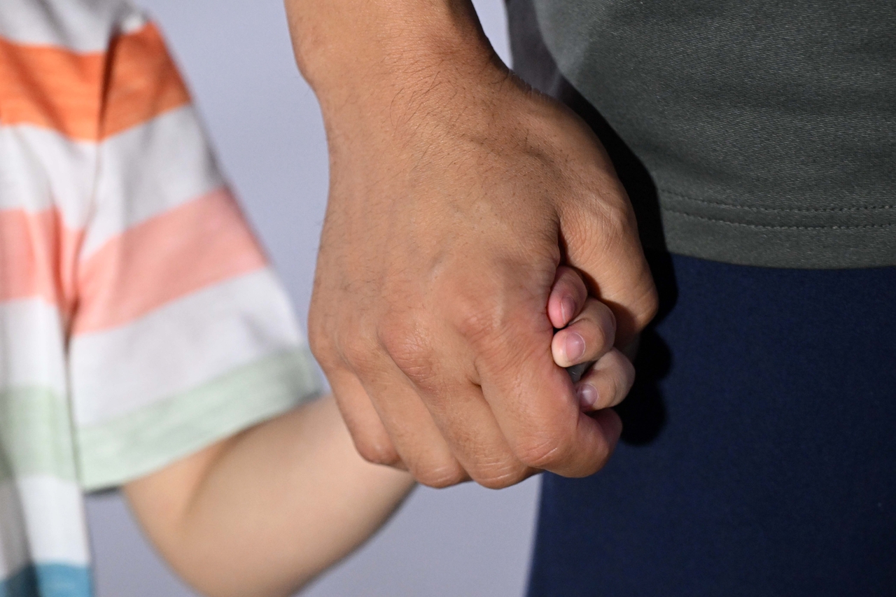 A South Korean national who returned home after being detained in the US holds hands with their child upon their arrival at the Incheon International Airport, Friday. (Joint Press Corps)