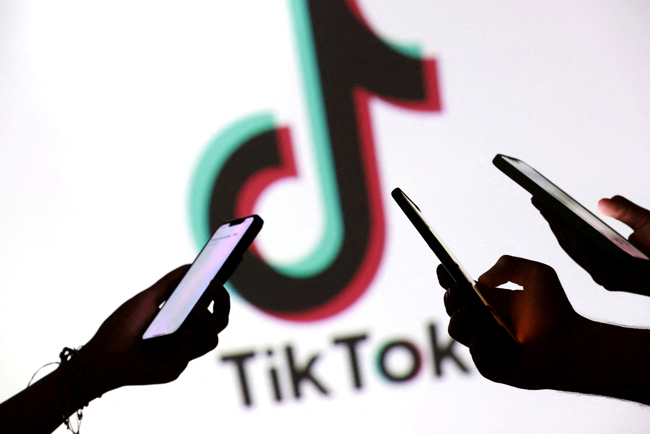 Teenagers pose for a photo while holding smartphones in front of a TikTok logo.   Reuters-Yonhap