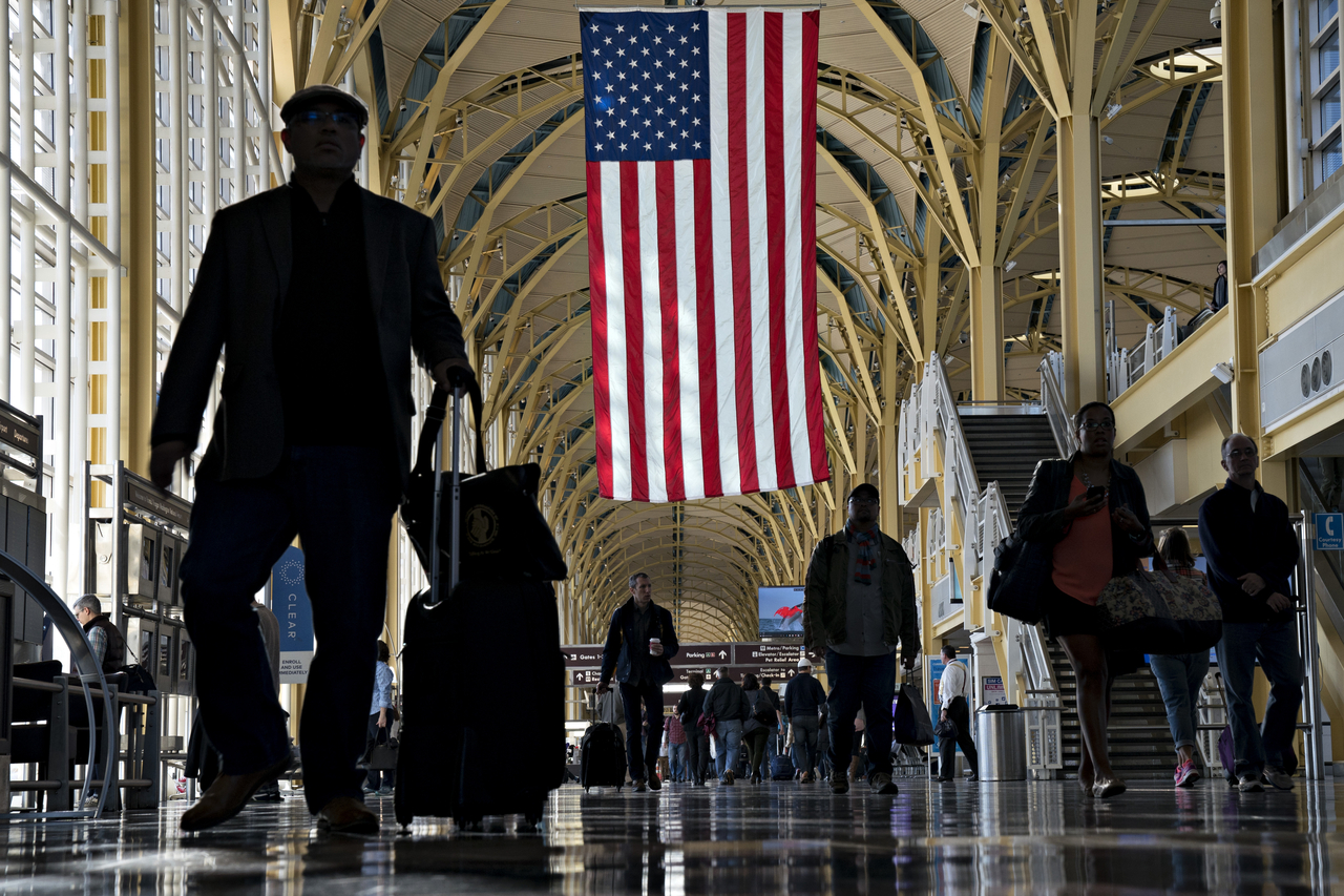 People walk underneath an American flag displayed at Ronald Reagan National Airport in Washington, Nov. 22, 2017.   Bloomberg