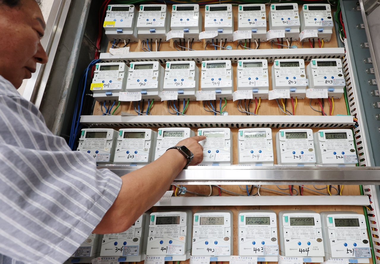 A worker inspects rows of electricity meters at a residential building in Seoul on July 15. Around that time, the government and ruling Democratic Party agreed to ease summer electricity rates to reduce household cooling costs. (Newsis)
