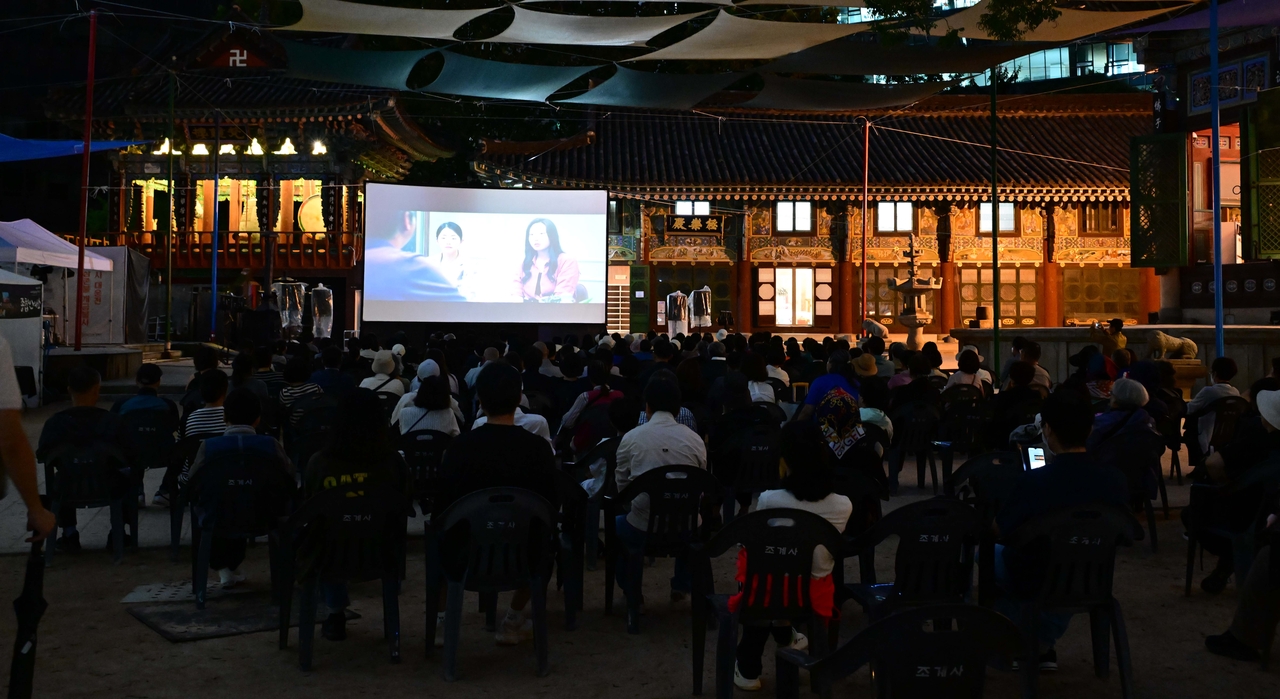 People watch "Mungyeong: More than Roads," the closing film of the One World, One Flower International Buddhist Film Festival, at the outdoor plaza of Daeungjeon Hall at Jogye Temple in central Seoul on Saturday evening. (Lee Sang-sub/The Korea Herald)