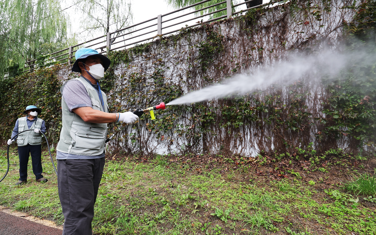 Health officials from a public health center in Suwon, Gyeonggi Province, carry out pest control operations along a path on Thursday. (Yonhap)