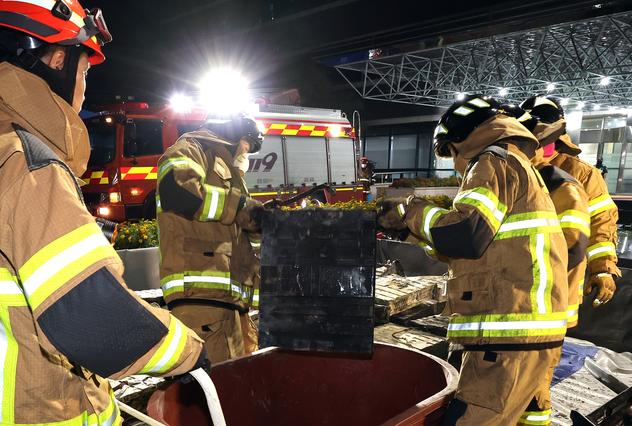 Firefighters move burnt lithium batteries into a tub on Saturday, in front of the National Information Resources Service's data center in Daejeon. (Yonhap)