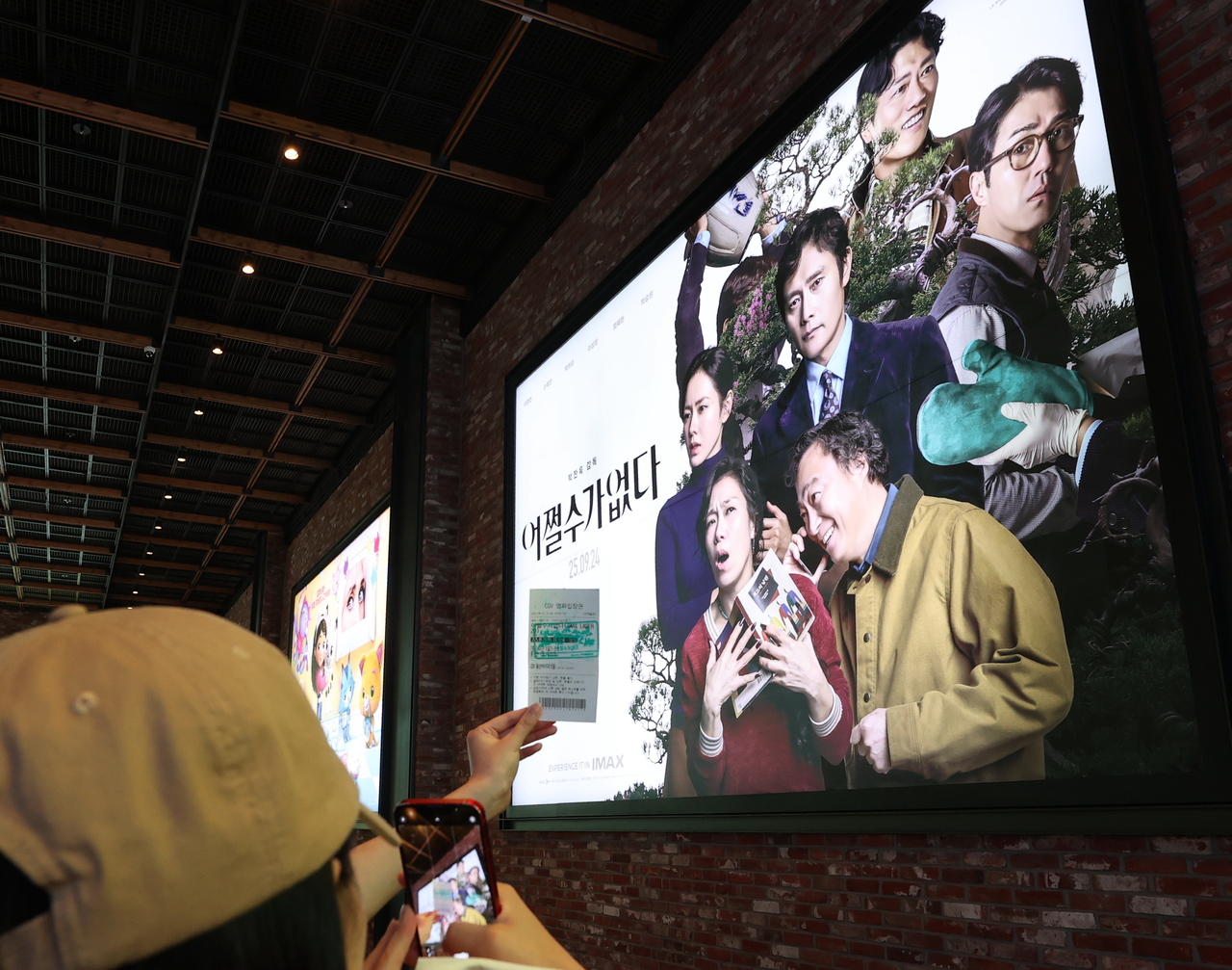 A moviegoer takes a photo of their ticket with a "No Other Choice" poster in the background at a Seoul cinema on Thursday. (Yonhap)