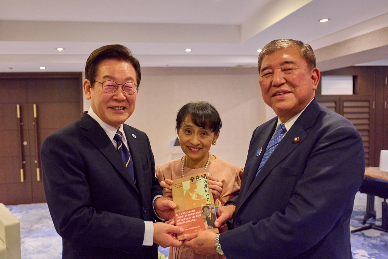 President Lee Jae Myung (left), Japanese Prime Minister Shigeru Ishiba (right) and his wife Yoshiko Ishiba pose with a Japanese edition of Lee’s book at the Westin Chosun in Busan, Tuesday. (Yonhap)