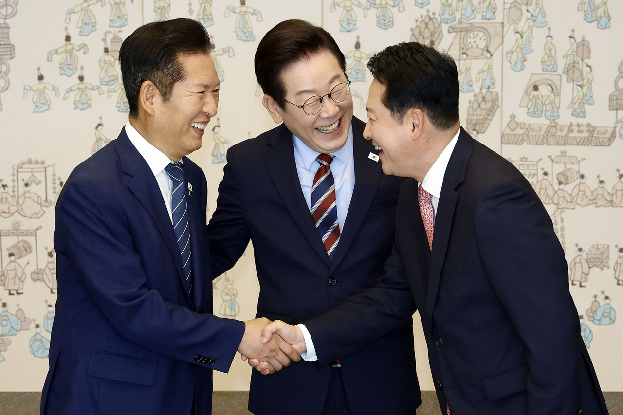 Democratic Party Chair Rep. Jung Chung-rae (left) and People Power Party Chair Rep. Jang Dong-hyeok (right) shake hands at a luncheon hosted by President Lee Jae Myung (center) at the presidential office in Yongsan-gu, central Seoul, on Monday. (Yonhap)