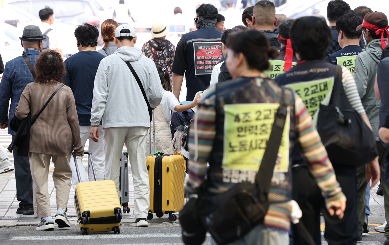 Striking airport workers walk alongside travelers outside the domestic terminal of Gimpo Airport in Seoul on Wednesday. (Yonhap)