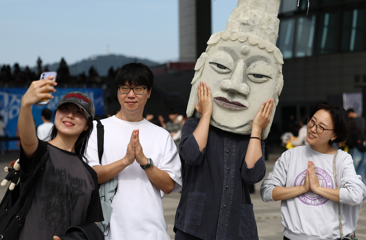 Visitors take a photo with a participant wearing a mask inspired by the stone-carved Buddha heads from the Unified Silla Dynasty (668-935) during an awards ceremony for a cosplay contest hosted by the National Museum of Korea, Saturday. (Yonhap)