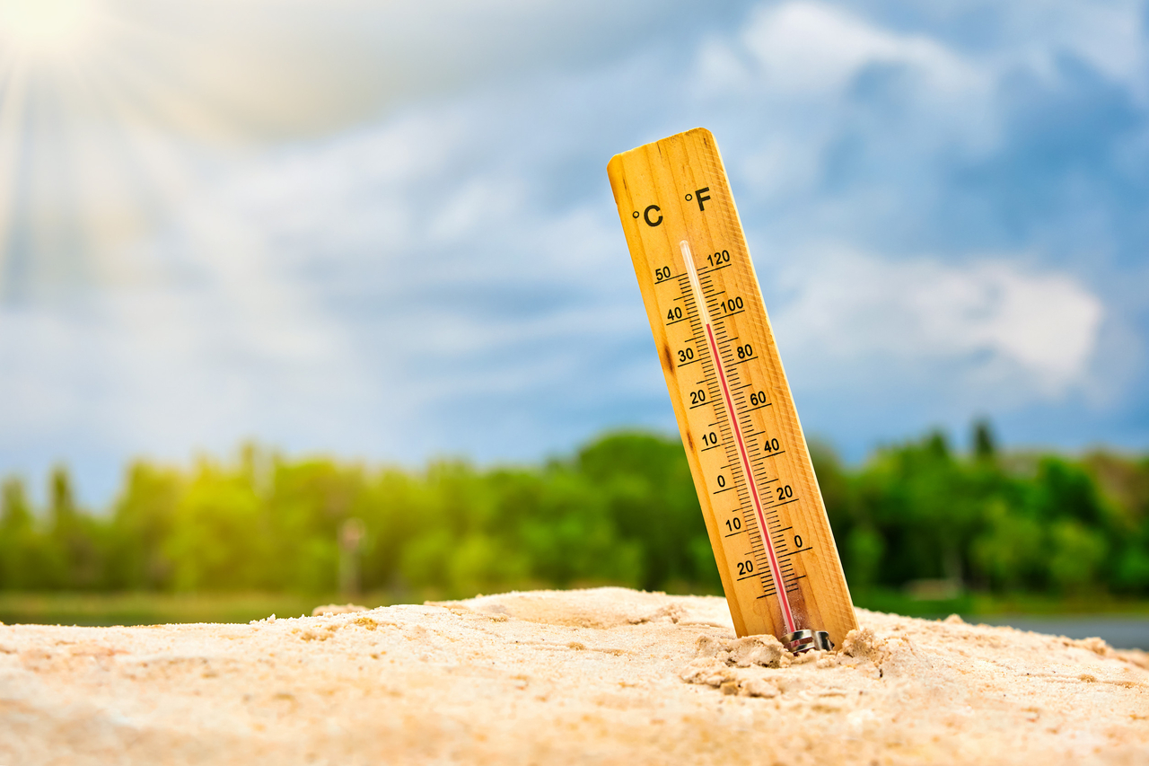 Weather thermometer in the sand against the sky showing a high ambient temperature (123rf)