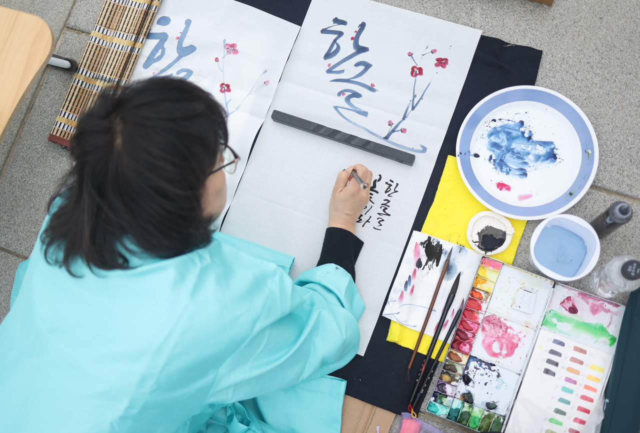 A woman paints a Hangeul phrase alongside illustrations of traditional Korean flowers at the 16th annual Gwanghwamun Square Calligraphy Competition in central Seoul on Thursday. (Yonhap)