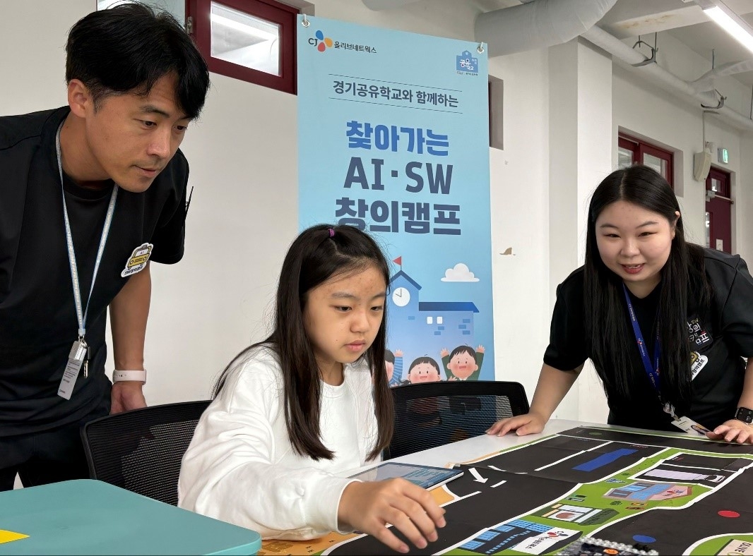A student participating in CJ OliveNetworks' 'Visiting AI & SW Creative Camp' checks the path of a self-driving car they coded, alongside employee instructors from the company (CJ OliveNetworks)