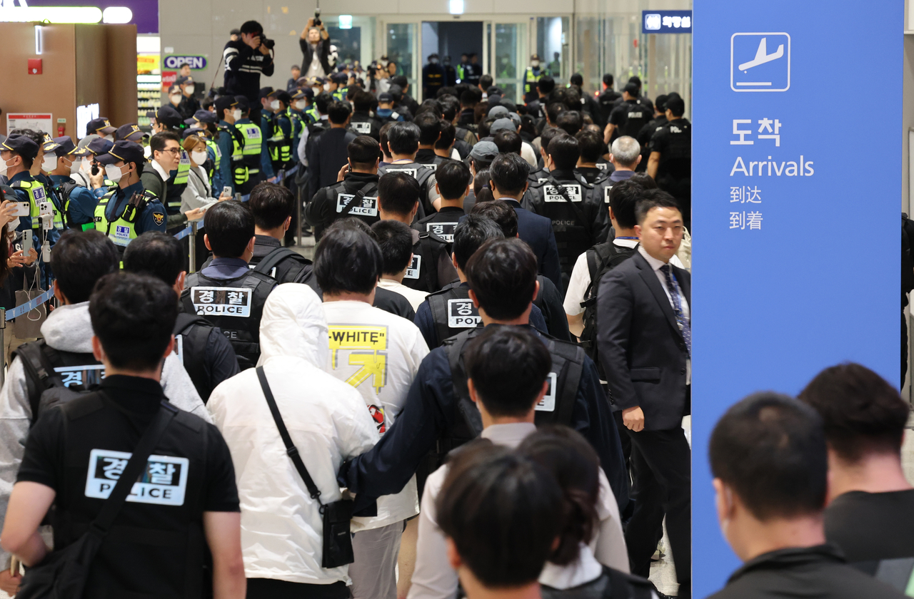 South Koreans detained in Cambodia for their involvement in online scams are escorted by police officers upon arrival at Incheon International Airport’s Terminal 2 on Saturday. (Yonhap)