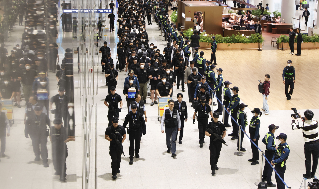 South Koreans involved in online scam operations in Cambodia are escorted by police officers upon arrival at Incheon International Airport’s Terminal 2 on Saturday morning. (Yonhap)