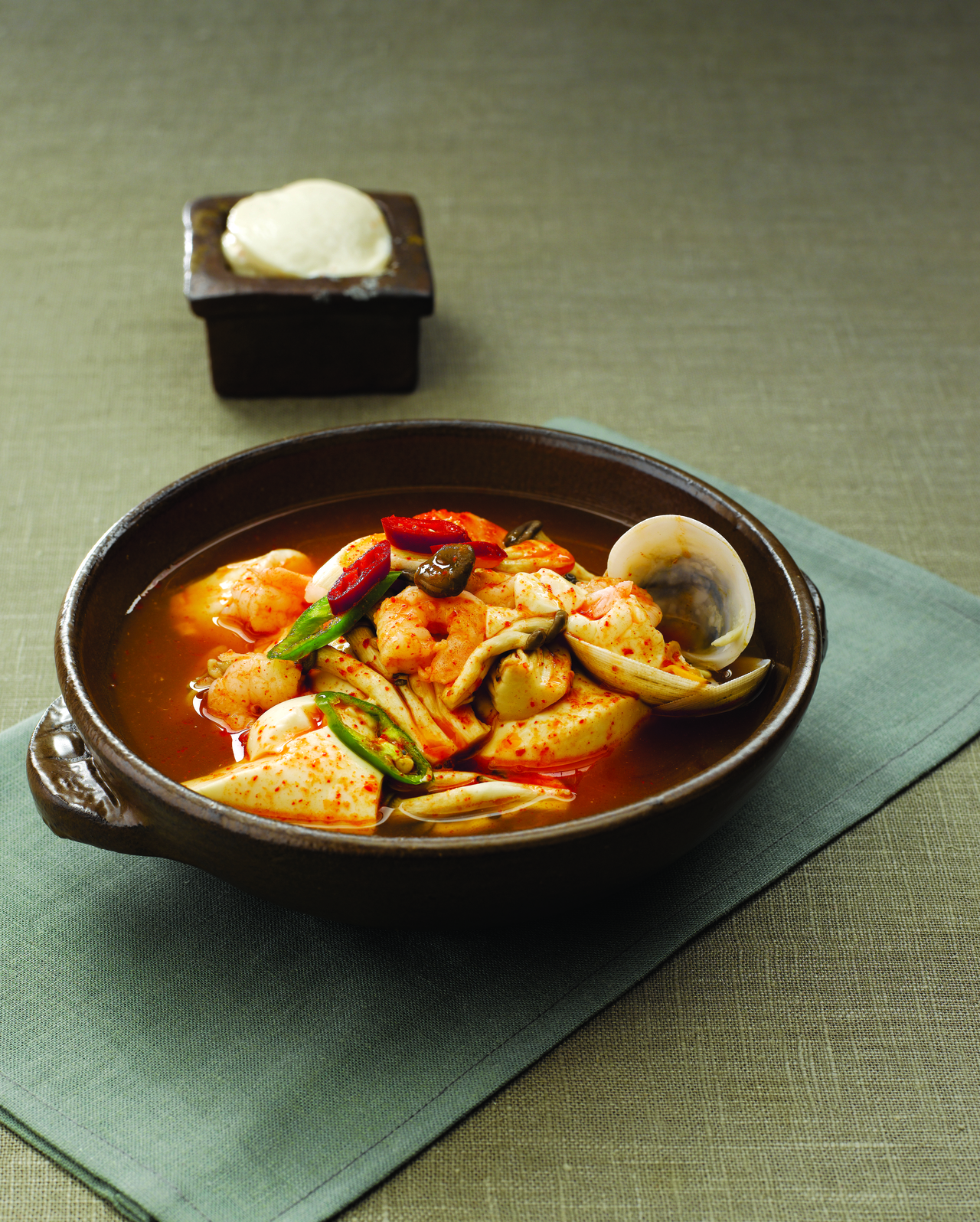 A bubbling earthenware pot of Korean sundubu jjigae soft tofu stew with pork oyster mushrooms and egg in a spicy red broth