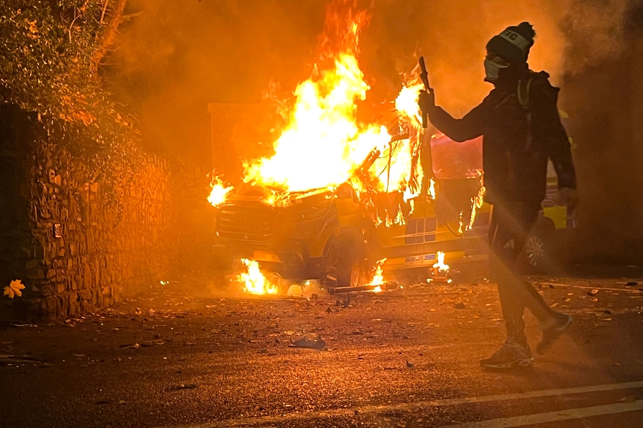 A protester films and a police vehicle burns in the background during a demonstration in Saggart, Dublin, Tuesday. (AFP-Yonhap)