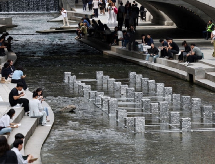 People relax along Cheonggyecheon stream in Jung-gu, central Seoul, showing the daylighted urban river surrounded by high-rises and greenery