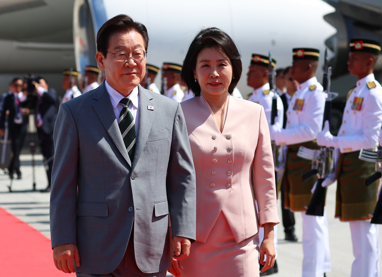 President Lee Jae Myung (left) and first lady Kim Hea Kyung walk on the red carpet upon their arrival at Kuala Lumpur International Airport in Kuala Lumpur, Malaysia, on Sunday, to attend the Association of Southeast Asian Nations summit. (Yonhap)
