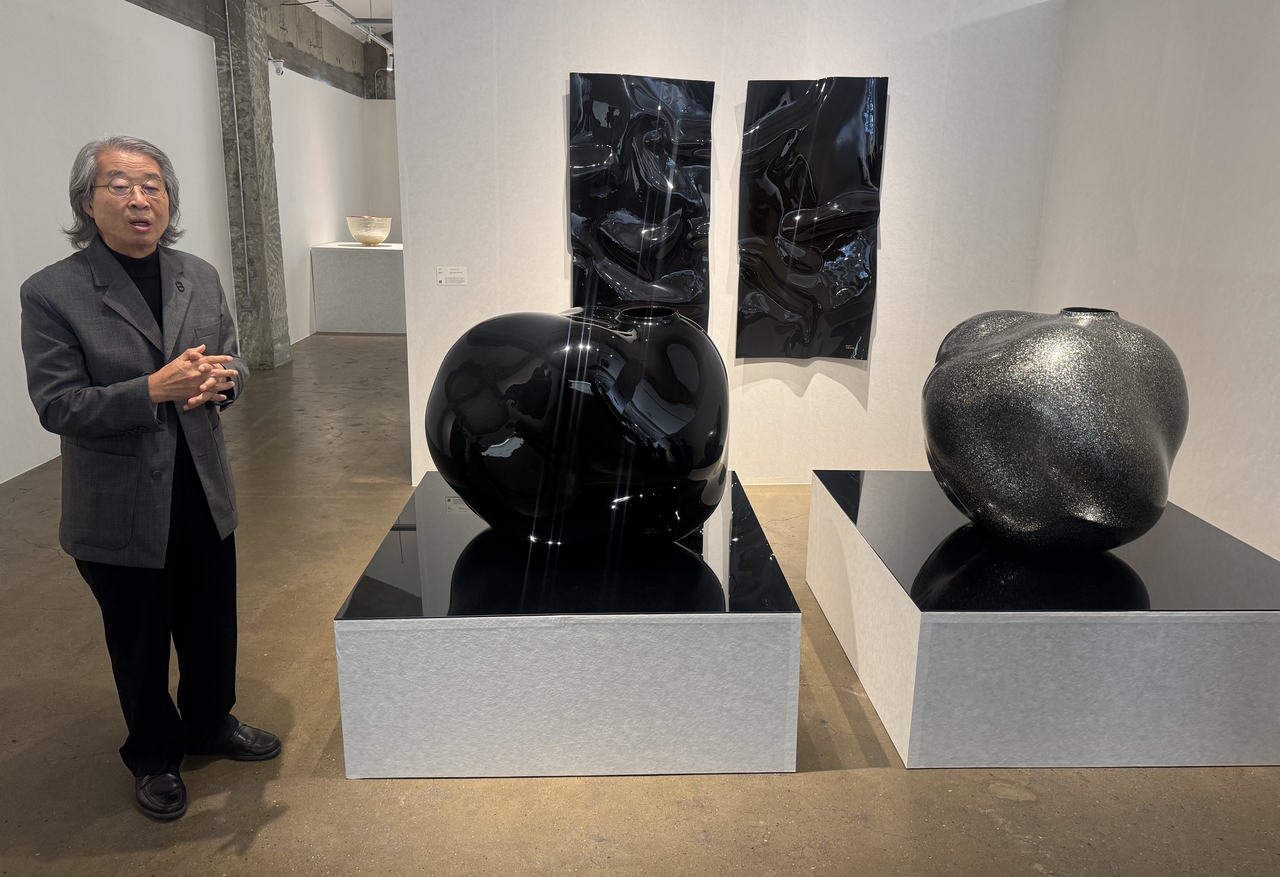 Chung Hae-cho, one of Korea's most prominent lacquerware artists, explains his works "Rhythm of the Red, Blue Lusters 2501" (displayed on the wall) and "Rhythm of the Monter-of-Pearl Black Luster 2203" (right) on Tuesday  at Cheongun Hybird Complex in Gyeongju, North Gyeongsang Province on Tuesday. (Park Ga-young/The Korea Herald)