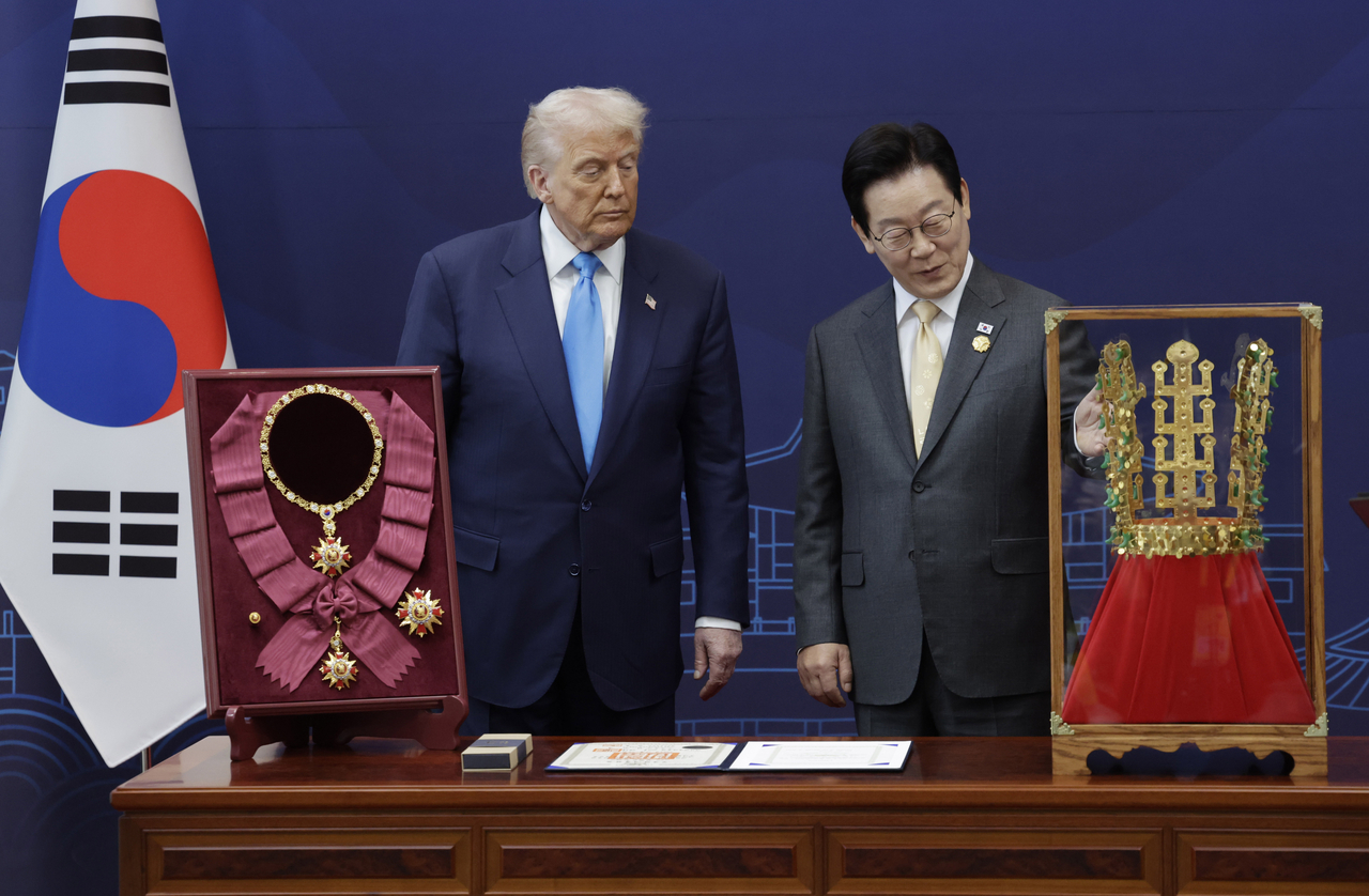 South Korean President Lee Jae Myung (right) shows US President Donald Trump a replica of the Cheonmachong gold crown, a gift prepared by the South Korean government. On the left side of the photo is the Grand Order of Mugunghwa, South Korea’s highest decoration. (Joint Press Corps via Yonhap)