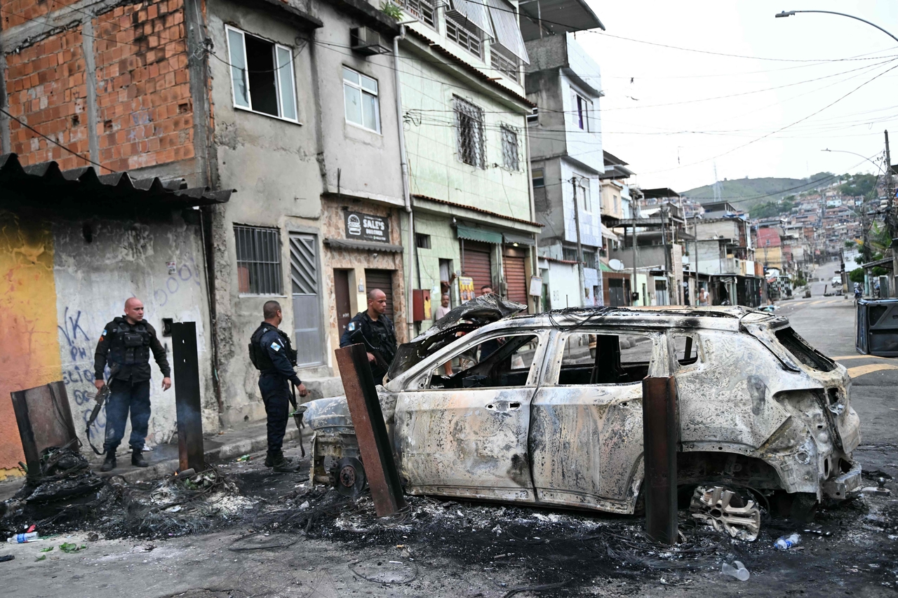 Police officers stand next to a burned car during an operation in Rio de Janeiro, Tuesday. (AFP-Yonhap)