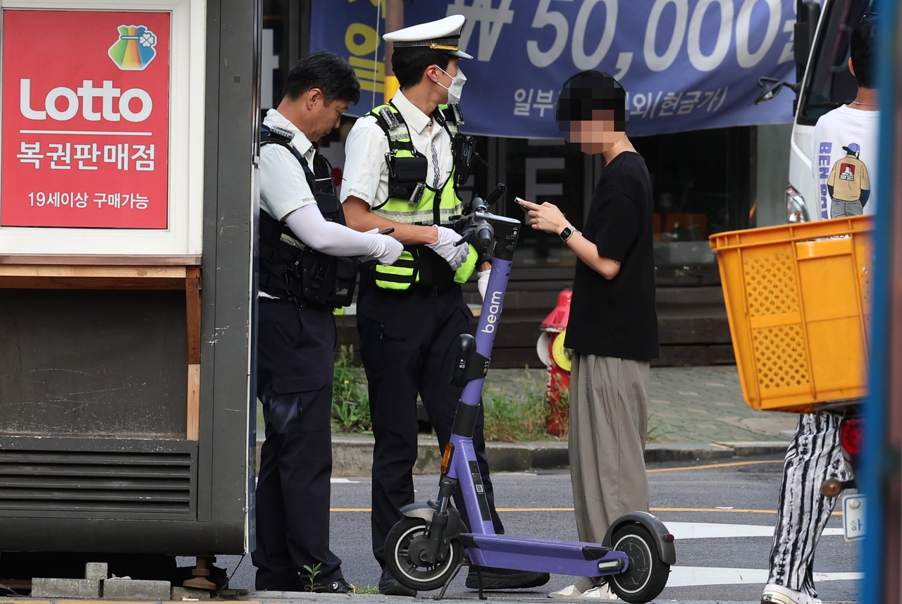 Officers in  Seong-dong, Seoul,  stop an e-scooter rider near Seongsu Station in August during a crackdown targeting helmet violations and rider safety. (Newsis)