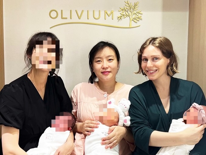 Cho Kyu-youn (center) and Sandra Meynier Kang (right) pose for a photo holding their babies at Olivium. (Courtesy of Olivium)