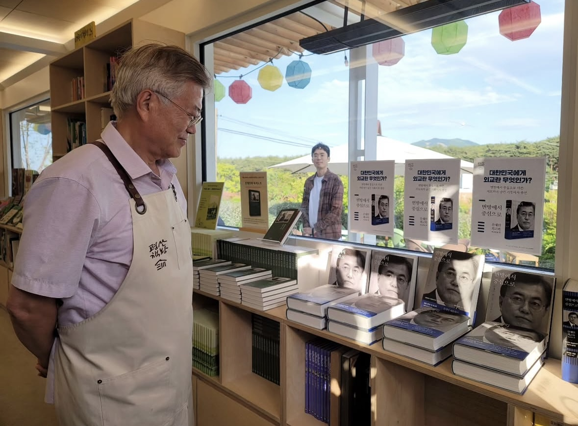Former President Moon Jae-in looks at copies of his memoir at his bookstore, the Pyeongsan Chaekbang, in May. (Instagram @moonjaein)