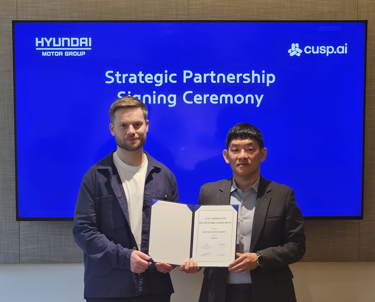 Park Chul (right), head of Hyundai Motor Group’s New Business Strategy Group, and Chad Edwards, CEO of CuspAI, hold a partnership certificate during a signing ceremony at CuspAI’s headquarters in Cambridge, UK, on Thursday. (Hyundai Motor Group)