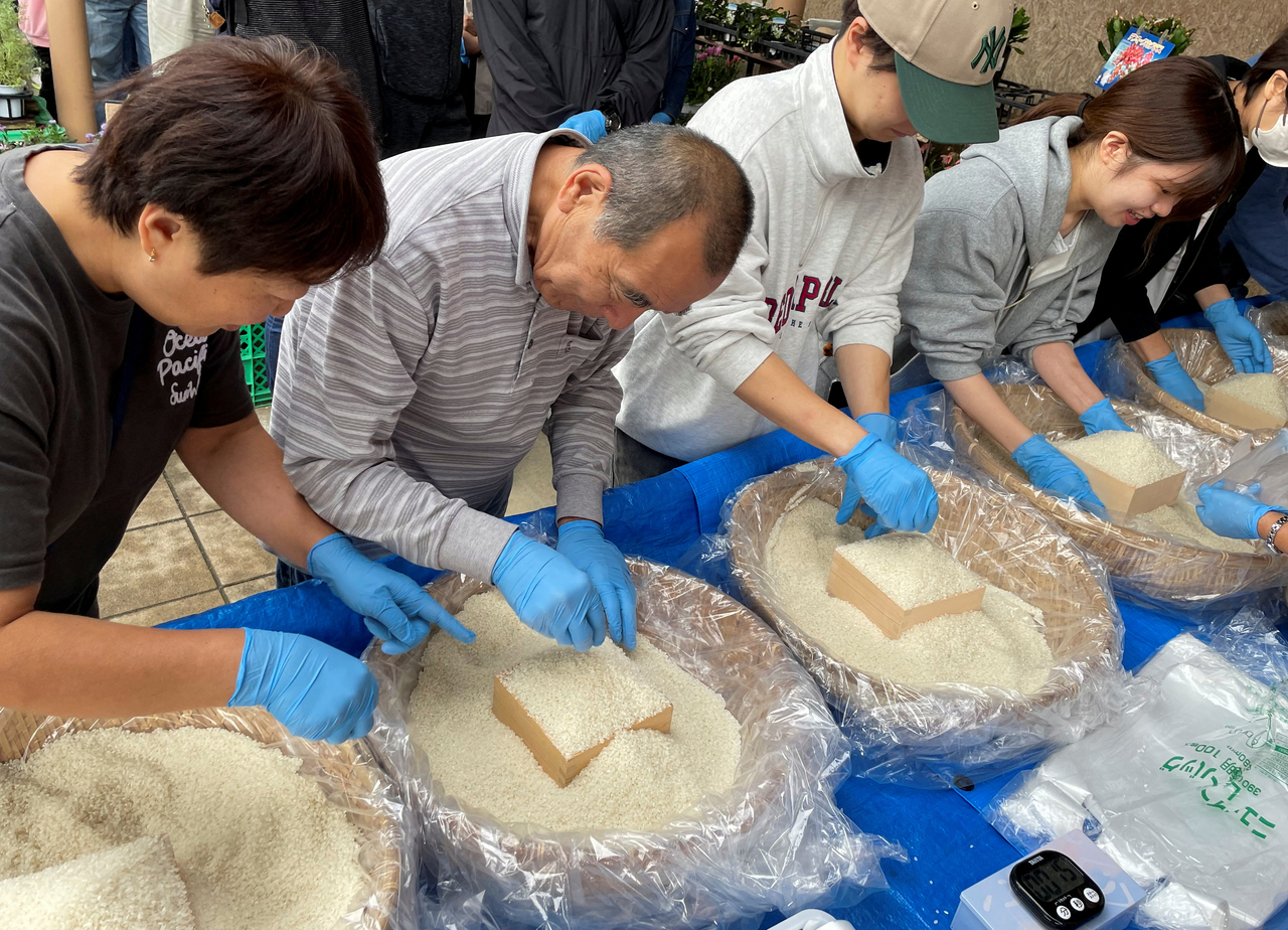 Shoppers take part in an event where they can take home as much rice as they can pile into a wooden box, at a farmer's market in Kisarazu, east of Tokyo, Oct. 12.   Reuters-Yonhap