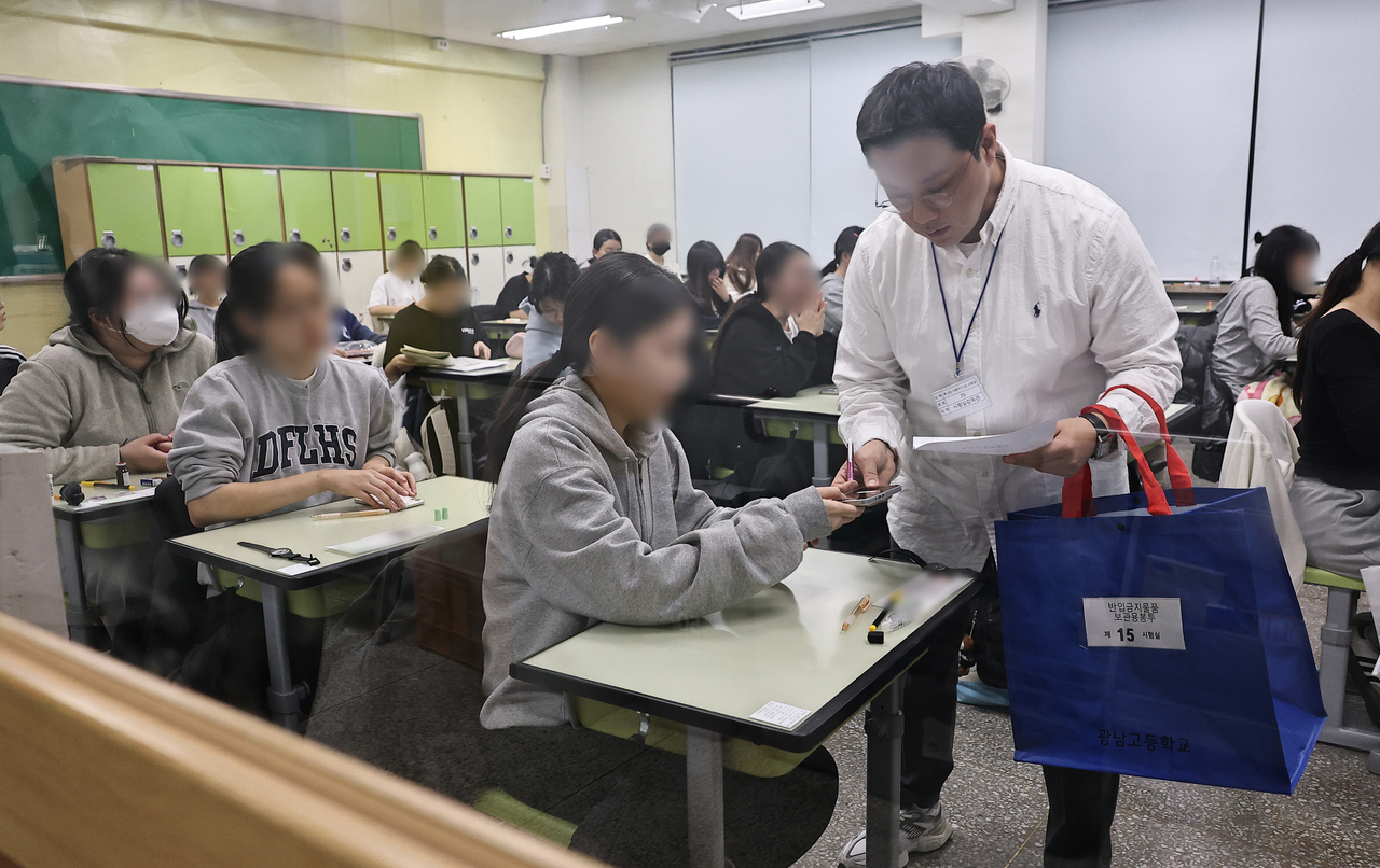 An exam supervisor collects students’ mobile phones at Gwangnam High School in Gwangjin-gu, Seoul, during the 2026 CSAT on Thursday. (Yonhap)