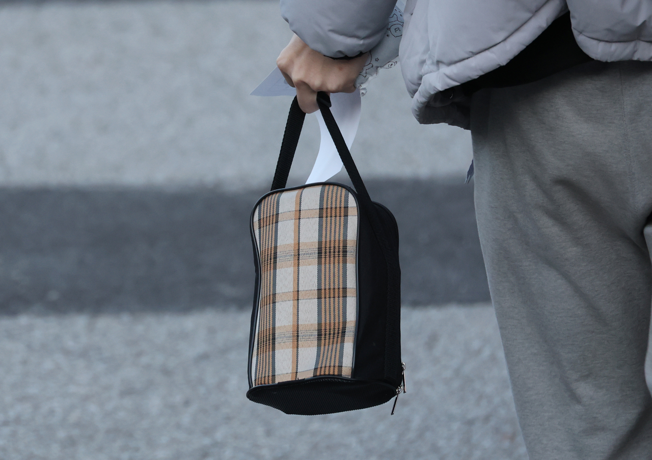 A student holding a lunch box and exam slip enters Jeonju Youngsaeng High School, which serves as Test Site No. 8 in District 67 under the North Jeolla Provincial Office of Education, on the day of the 2026 CSAT, Thursday (Yonhap)