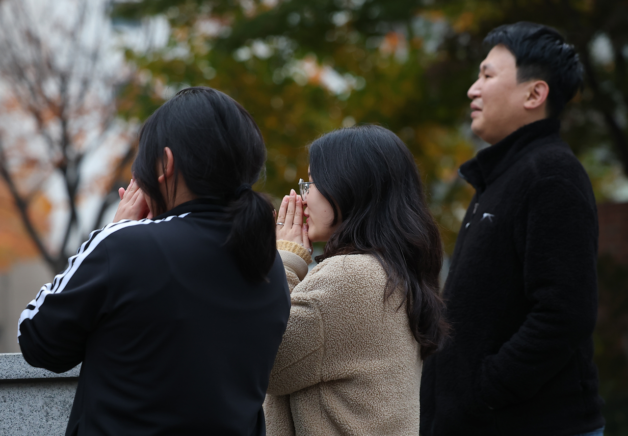 A family prays in front of Ewha Girls’ Foreign Language High School in Jung-gu, Seoul, where the 2026 CSAT was held on Thursday. (Yonhap)