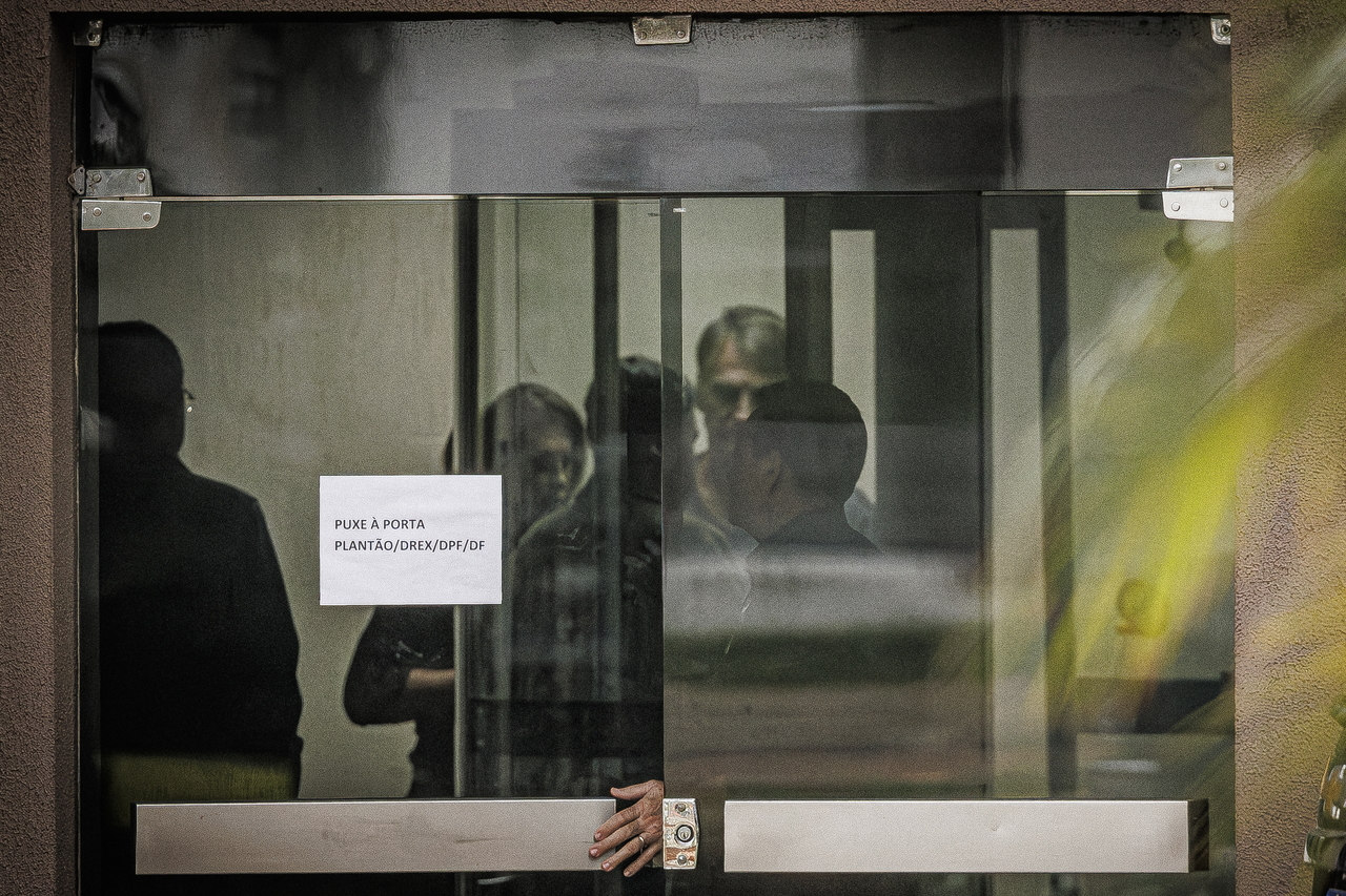 Former Brazilian President Jair Bolsonaro (rear in right) stands behind a glass door at Federal Police headquarters in Brasilia, Brazil, Sunday. (EPA-Yonhap)