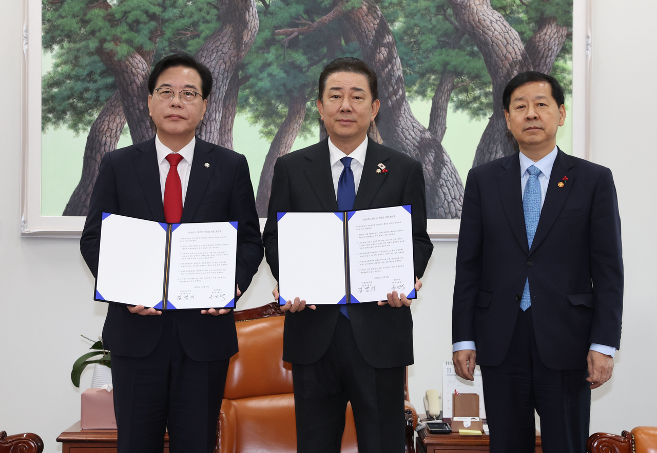 Rep. Kim Byung-kee (center), floor leader of the ruling Democratic Party of Korea, and Rep. Song Eon-seog (left), floor leader of the main opposition People Power Party, hold the agreement on the 2026 budget bill as they pose for a photo alongside Deputy Prime Minister and Finance Minister Koo Yun-cheol at the National Assembly in Seoul on Tuesday. (Yonhap)